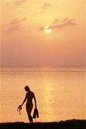 Seven Mile Beach, Grand Cayman Island. A silhouetted woman with swim flippers walking a beach at sunset. (Photo by Michael Lewis/National Geographic/Getty Images)